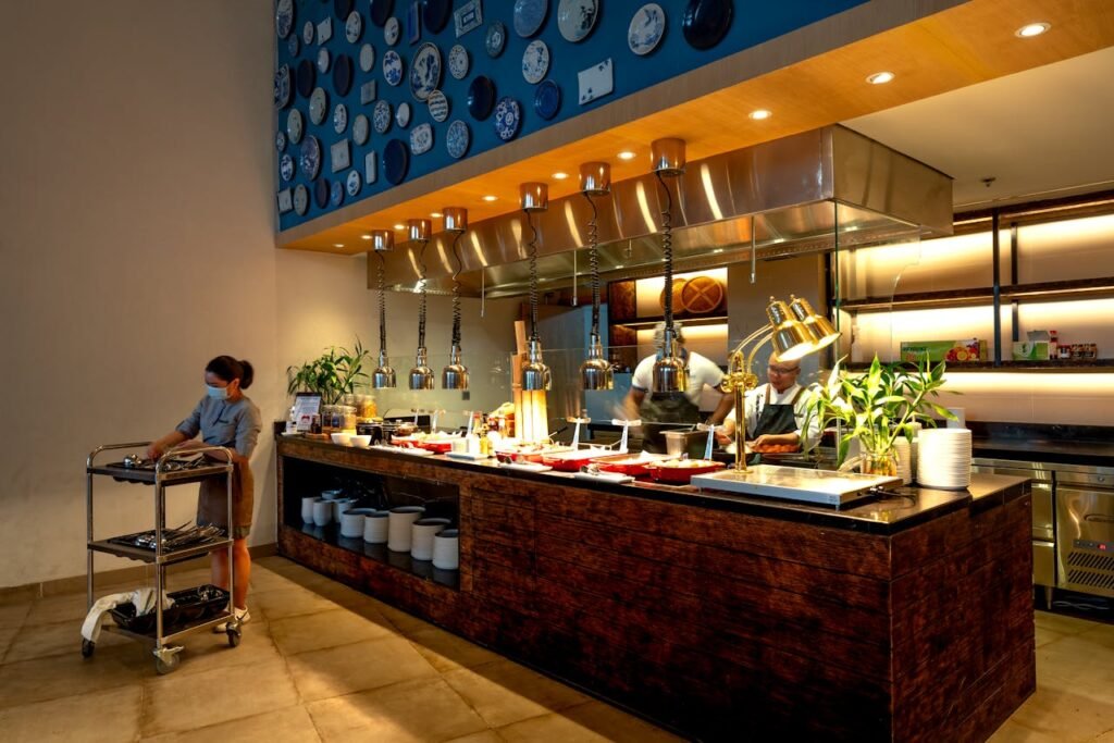 Modern restaurant kitchen with chefs preparing food and waitress on side.